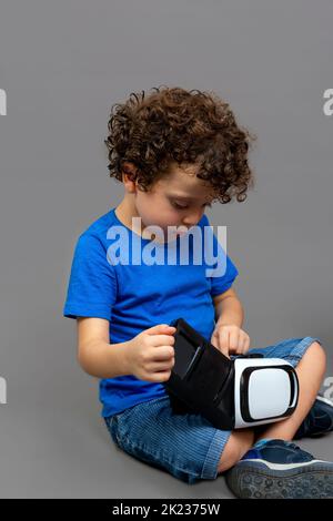 Kind mit einer Virtual-Reality-Brille in den Händen, das neugierig auf ihre Arbeitsweise schaut Stockfoto