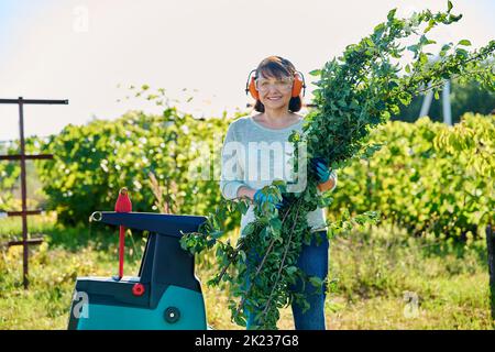 Frau, die elektrischen Gartenschredder für Äste und Sträucher verwendet Stockfoto