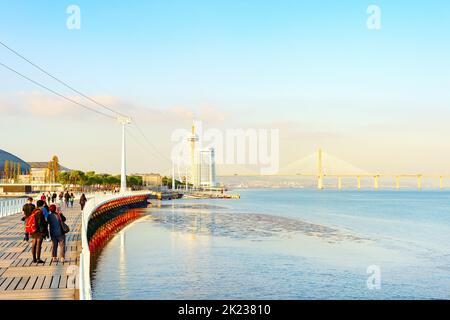 LISSABON, PORTUGAL - 11. NOVEMBER 2021: Vasco da Gama Brücke und Hotel moderner futuristischer Architektur, Menschen an der Promenade im Abendlicht, Lissabon, P Stockfoto