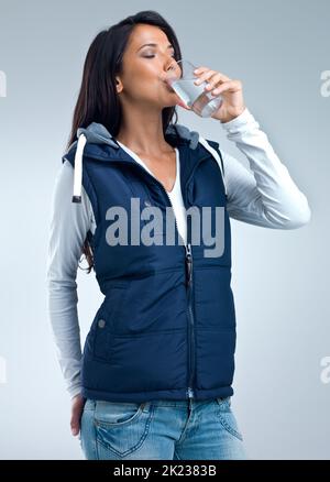 Ihren Durst löschen. Eine Studioaufnahme einer schönen Frau, die ein Glas Wasser trinkt. Stockfoto