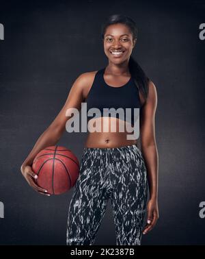 Lasst uns Basketball spielen. Studioaufnahme einer schönen jungen Frau, die einen Basketball vor schwarzem Hintergrund hält. Stockfoto