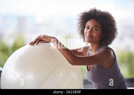 Das ist mein Fitnessgeheimnis. Ein Porträt einer attraktiven jungen Frau, die mit einem Gymnastikball sitzt. Stockfoto