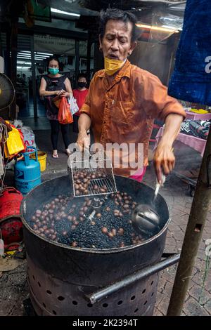 Malaysia, 10. Juli 2022 - der Mann sammelt geröstete Kastanien im Imbissstand am offenen Brunnen. Stockfoto