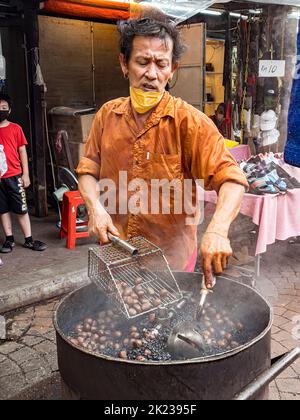 Malaysia, 10. Juli 2022 - der Mann sammelt geröstete Kastanien im Imbissstand am offenen Brunnen. Stockfoto