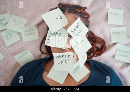 Schwarze Frau auf dem Bett, Haftnotiz auf dem Gesicht für Motivation und Erfolg im Leben. Afrikanische Dame im Schlafzimmer, kleben Sie Papier mit Fragen auf Haut und Augen Stockfoto