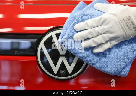 Zwickau, Deutschland. 26. April 2022. Ein Mitarbeiter wischt im Lichttunnel im Volkswagen-Werk in Zwickau das VW-Logo auf einer ID.4 ab. Neben VW-Fahrzeugen kommen im Werk auch Fahrzeuge der Marken Audi und Seat vom Band. Die Fahrzeuge basieren auf dem Modular Electric Toolkit. Volkswagen hat den rund 9.000 Mitarbeiter beschäftigende Standort zu einem reinen Elektrofahrzeugwerk für 1,2 Milliarden Euro umgebaut. Quelle: Jan Woitas/dpa/Alamy Live News Stockfoto