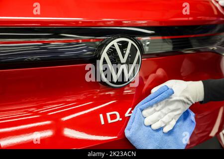 Zwickau, Deutschland. 26. April 2022. Ein Mitarbeiter wischt im Lichttunnel im Volkswagen-Werk in Zwickau das VW-Logo auf einer ID.4 ab. Neben VW-Fahrzeugen kommen im Werk auch Fahrzeuge der Marken Audi und Seat vom Band. Die Fahrzeuge basieren auf dem Modular Electric Toolkit. Volkswagen hat den rund 9.000 Mitarbeiter beschäftigende Standort zu einem reinen Elektrofahrzeugwerk für 1,2 Milliarden Euro umgebaut. Quelle: Jan Woitas/dpa/Alamy Live News Stockfoto
