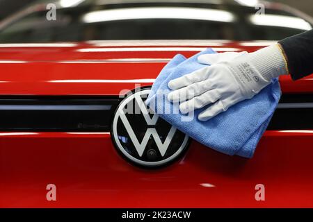 Zwickau, Deutschland. 26. April 2022. Ein Mitarbeiter wischt im Lichttunnel im Volkswagen-Werk in Zwickau das VW-Logo auf einer ID.4 ab. Neben VW-Fahrzeugen kommen im Werk auch Fahrzeuge der Marken Audi und Seat vom Band. Die Fahrzeuge basieren auf dem Modular Electric Toolkit. Volkswagen hat den rund 9.000 Mitarbeiter beschäftigende Standort zu einem reinen Elektrofahrzeugwerk für 1,2 Milliarden Euro umgebaut. Quelle: Jan Woitas/dpa/Alamy Live News Stockfoto