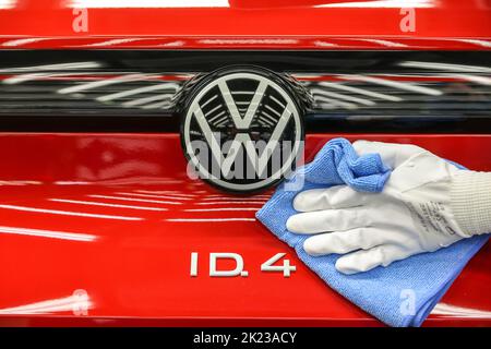Zwickau, Deutschland. 26. April 2022. Ein Mitarbeiter wischt im Lichttunnel im Volkswagen-Werk in Zwickau das VW-Logo auf einer ID.4 ab. Neben VW-Fahrzeugen kommen im Werk auch Fahrzeuge der Marken Audi und Seat vom Band. Die Fahrzeuge basieren auf dem Modular Electric Toolkit. Volkswagen hat den rund 9.000 Mitarbeiter beschäftigende Standort zu einem reinen Elektrofahrzeugwerk für 1,2 Milliarden Euro umgebaut. Quelle: Jan Woitas/dpa/Alamy Live News Stockfoto