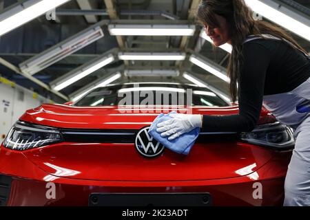 Zwickau, Deutschland. 26. April 2022. Ein Mitarbeiter wischt im Lichttunnel im Volkswagen-Werk in Zwickau das VW-Logo auf einer ID.4 ab. Neben VW-Fahrzeugen kommen im Werk auch Fahrzeuge der Marken Audi und Seat vom Band. Die Fahrzeuge basieren auf dem Modular Electric Toolkit. Volkswagen hat den rund 9.000 Mitarbeiter beschäftigende Standort zu einem reinen Elektrofahrzeugwerk für 1,2 Milliarden Euro umgebaut. Quelle: Jan Woitas/dpa/Alamy Live News Stockfoto