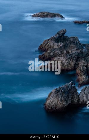 Lange Exposition von Meer und Felsen. Wellen, die auf den Felsen plätschern, schaffen ein schönes Bild. Wunderschöne Farben bei Sonnenuntergang. Asturien-Landschaft Stockfoto