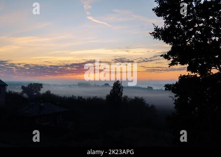 Panoramablick auf die bunte Dämmerung über dem Fluss mit Nebel am frühen Sommermorgen. Hochwertiges FotoPanoramablick auf die farbenfrohe Dämmerung über dem Fluss mit Nebel am frühen Sommermorgen. Stockfoto