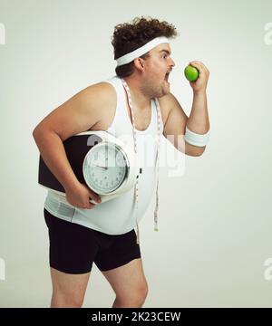 Fit für das Leben. Ein übergewichtiger Mann hält einen Apfel, Waage und Maßband. Stockfoto
