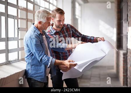 Jeder anfängerliche Architekt braucht eine helfende Hand. Zwei männliche Architekten diskutieren Baupläne, während sie drinnen stehen. Stockfoto