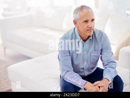 Ein reifer Mann sitzt tief in Gedanken auf seinem Sofa. Stockfoto