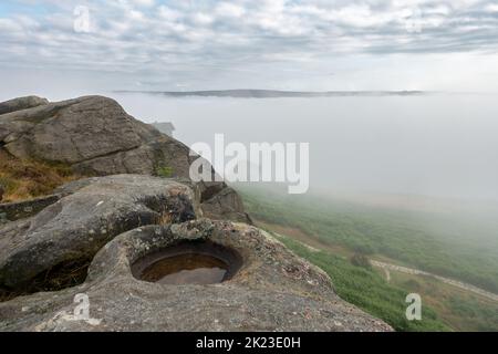 Eine Wolkeninversion in Wharfedale führt zu einem nebelgefüllten Tal und einem stimmungsvollen Blick auf die Cow und Calf Rocks auf Ilkley Moor, West Yorkshire, Englan Stockfoto
