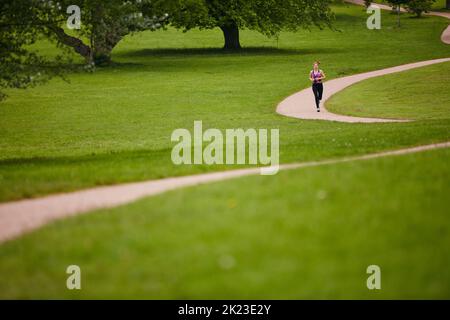 Der perfekte Ort zum Joggen. Eine Frau, die auf einem Fußpfad in einem Park joggt. Stockfoto