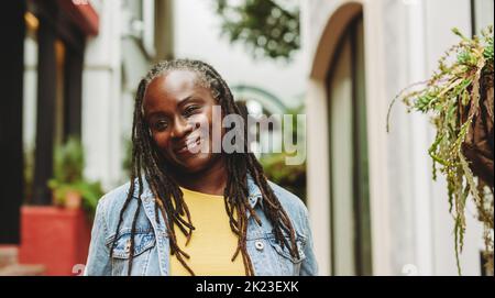 Frau mit Dreadlocks lächelt fröhlich, während sie draußen steht. Fröhliche ältere Frau, die in legerer Kleidung ausgeht. Stockfoto