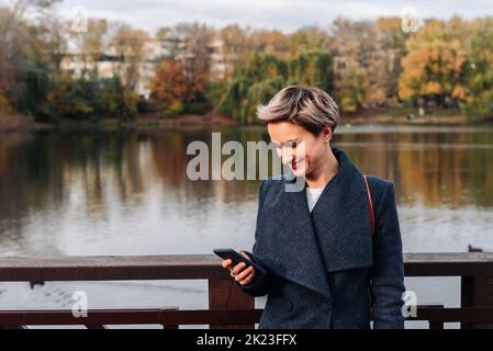 Eine Frau in einem Stadtpark am Fluss nutzt ein Smartphone Stockfoto