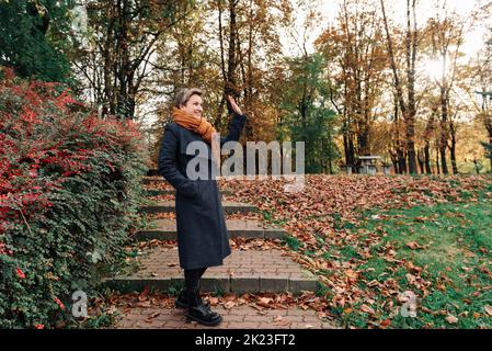 Eine junge Frau winkt im Herbst im Park mit der Hand Stockfoto