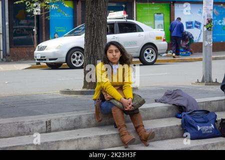 La Paz, Bolivien - 11 2022. September: Auf der Tribüne der Straße sitzt eine junge bolivianische Frau in einem gelben Pullover Stockfoto