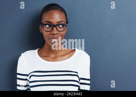 Shes hat ihr Auge auf dich gerichtet. Eine attraktive junge Frau trägt eine Brille, die seitlich auf einem grauen Hintergrund sieht. Stockfoto