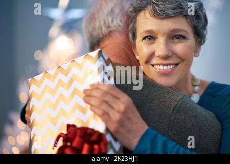 Die Liebe zu weihnachten verbreiten. Porträt einer reifen Frau, die ihrem Partner für ihr weihnachtsgeschenk mit einer Umarmung dankt. Stockfoto