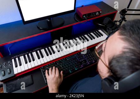Draufsicht auf den jungen kaukasischen Musikproduzent, der Brillen trägt, Monitor beobachtet und Computertastatur in seinem Musikstudio Music Indu tippt Stockfoto
