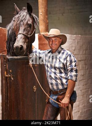 Es ist Zeit für eine Fahrt. Eine fürsorgliche Ranch Hand, die sich um ein Pferd im Stall kümmert. Stockfoto