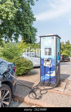 Schottland Glasgow - 19. Juli 2022: Laden eines Elektroautos auf einem öffentlichen Parkplatz mit Ladestation für Elektroautos Stockfoto