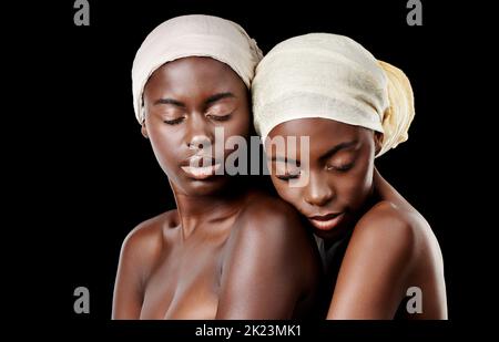 Ich fühle mich sicher bei meiner Schwester. Studioaufnahme von zwei schönen Frauen, die Kopftücher auf schwarzem Hintergrund tragen. Stockfoto