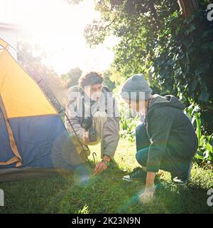 Ein Vater und sein kleiner Sohn, die ihr Zelt aufschlagen, schruppen es in freier Wildbahn. Stockfoto