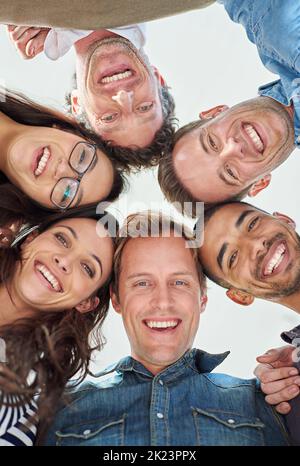 Mit unserer positiven Einstellung gewinnen. Beschnittene Aufnahme aus dem niedrigen Winkel von sechs Personen, die ihre Köpfe in einem Kreis zusammenfügen. Stockfoto