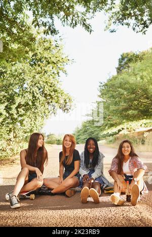 Lachen ist ein sofortiger Urlaub. Eine Gruppe von multirassischen Teenagern, die draußen sitzen und sich gegenseitig Gesellschaft genießen. Stockfoto
