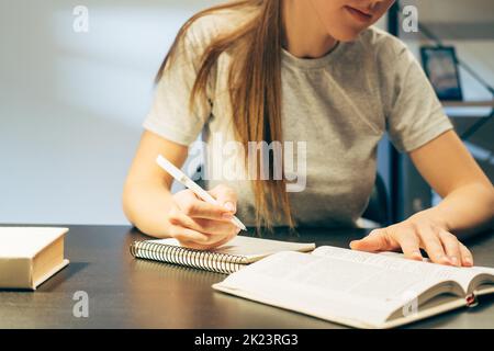 Selbstbildung. Fernunterricht. Pandemien sperren den Lebensstil. Das studentische Mädchen schrieb sich spät in der Nacht Notizen aus dem Buch an der Rezeption Stockfoto