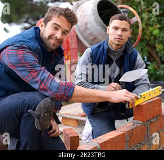 Starke Mauern und Bindungen. Porträt eines Maurersoluns und seines Lehrlings bei der Arbeit. Stockfoto