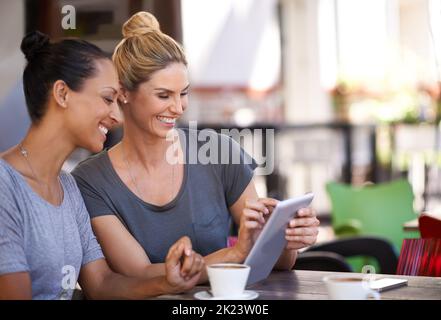 Technologie bringt Menschen näher. Zwei junge Frauen, die in einem Café ein Tablet betrachten. Stockfoto