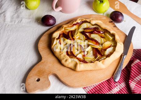 Hausgemachte Galette mit Apfel und Pflaume auf einer weißen Leinentischdecke. Öffnen Sie die PIE. Blick von oben auf hausgemachte Tortenkruste auf dem Tisch. Rustikale hausgemachten Obstkuchen. Stockfoto