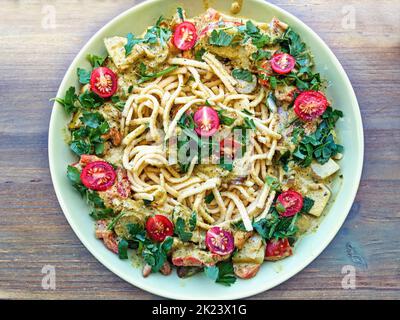 Draufsicht auf einen Teller mit Spätzle, umgeben von einem Rand aus Gemüsekerl, frischen Kräutern und halbierten Kirschtomaten. Stockfoto