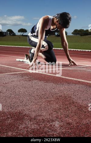 Bereit, gegen die Zeit zu Rennen. Ein junger Athlet, der auf einem Startblock meditiert. Stockfoto