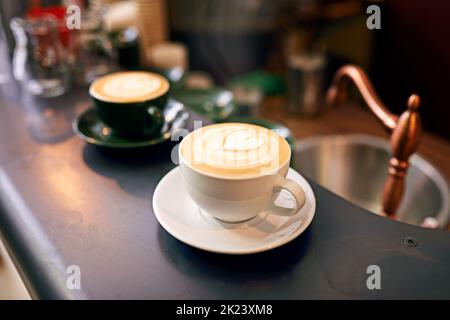 Café-Kultur. Hochgedrehte Aufnahme einer liebevoll zubereiteten Tasse Cappuccino, die auf einem Kaffeetisch sitzt. Stockfoto