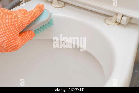Mann Hand in orange Handschuh mit einer Bürste reinigt Toilette. Stockfoto