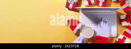 Weihnachtsverkauf, Vorbereitung für Urlaub Konzept. Weihnachtsmann Hände mit Laptop, heiße Schokolade Latte Tasse, Geschenk-Boxen, flach liegen auf goldenem Hintergrund. M Stockfoto