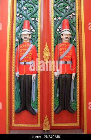 Farbenfrohe Holztür im alten Stil mit geschnitzten Soldaten als Wächter an Doppeltüren am Eingang zu einem alten Tempel. Stockfoto