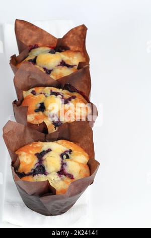 Eine Reihe frisch gebackener Blaubeer-Muffins im Papiertörtchen-Halter auf weißem Papiertaschenpapier Stockfoto