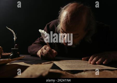 Senior Abt schreiben Manuskript auf Pergament isoliert auf schwarzem, Stock Bild Stockfoto