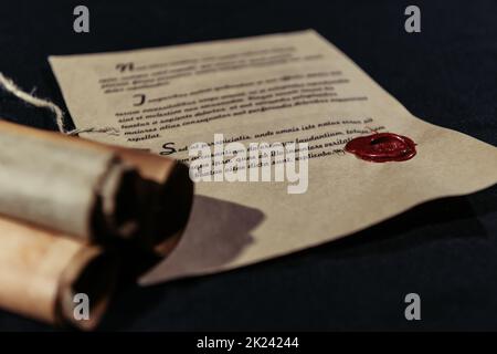 Manuskript mit Wachssiegel in der Nähe von gerollten Pergamenten auf schwarzem Hintergrund gestempelt, Stockbild Stockfoto