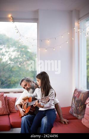 Ein kleines Mädchen, das mit ihrem Großvater Gitarre spielt. Stockfoto