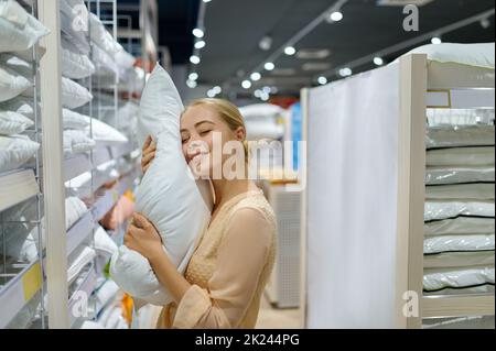 Lächelnd zufriedene Kundin hält flauschiges Kissen und kauft Waren in der Boutique des Heimtextilien-Shops Stockfoto