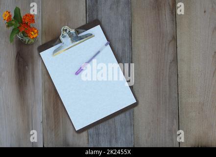 Zwischenablage mit leerem Blatt Papier auf Holztisch mit Blumen Flachbild Stockfoto